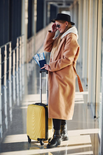 Young female passenger in warm clothes with tickets and baggage in airport hall. - Foto, immagini