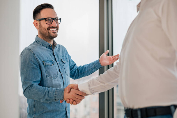 Businessman greeting job applicant businessmen handshaking over signed contract handsome entrepreneur handshake with a colleague cheerful young manager handshake with new employee getting a deal done. - Фото, изображение