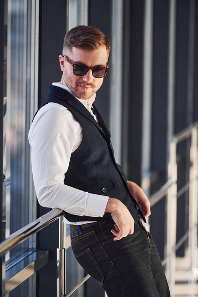 Man in elegant clothes and sunglasses is standing indoors and posing for the camera. - Foto, immagini