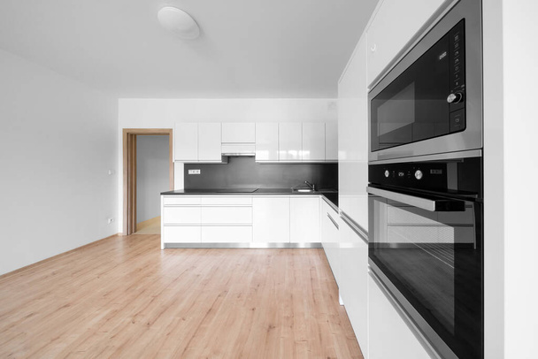 Celadna, Czechia - 05.07.2022: Empty room with wooden floor and white and black modern design kitchen. White walls and ceiling. - Foto, Imagem