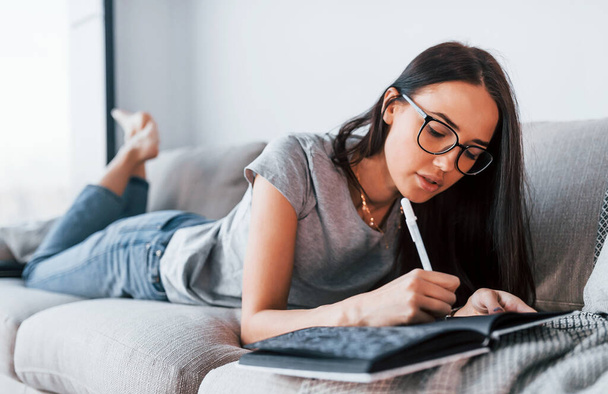 Young beautiful woman in casual clothes lying down at home alone with notepad and pen. - Foto, immagini