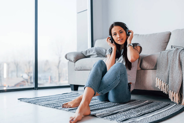 Young beautiful woman in casual clothes sitting at home alone and listening to the music in headphones. - Foto, afbeelding