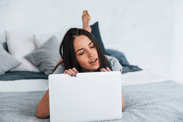 Young beautiful woman in casual clothes lying down at home alone with laptop. - Foto, Bild