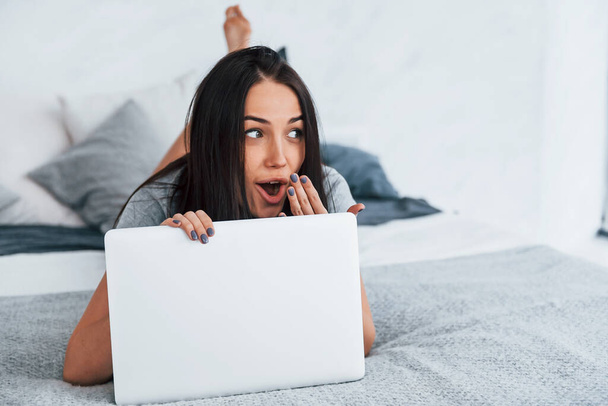 Young beautiful woman in casual clothes lying down at home alone with laptop. - Zdjęcie, obraz