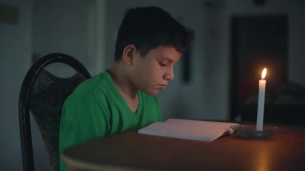 dítě sedí čtení u stolu se svíčkou - Záběry, video