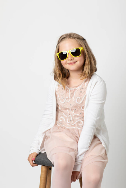 Little young teen girl, posing mischievously in the studio. The background is white and she has green sunglasses that are really too big for her. - Foto, Bild