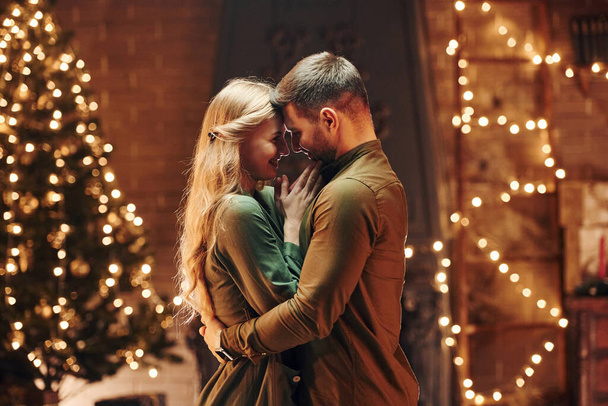 Standing in the Christmas decorated room. Young lovely couple have romantic dinner indoors together. - Φωτογραφία, εικόνα