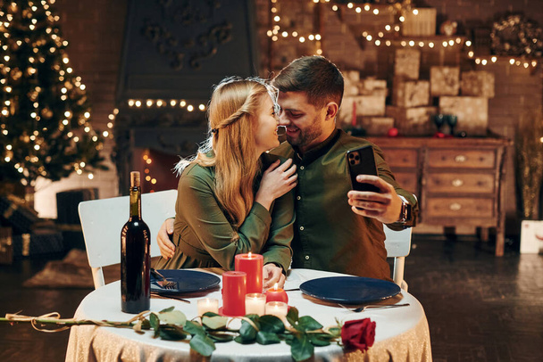 Making selfie by using phone. Young lovely couple have romantic dinner indoors together. - Zdjęcie, obraz