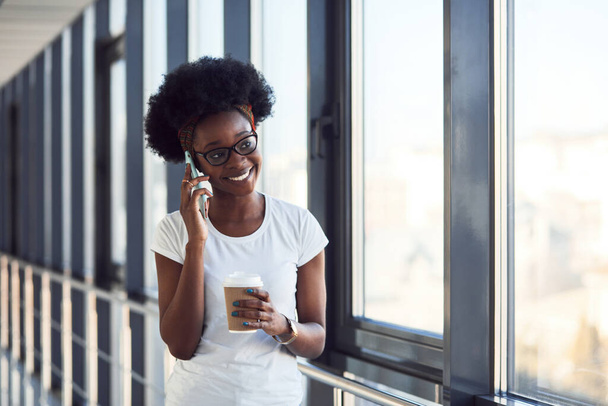 Joven afroamericano pasajero femenino en ropa casual está en el aeropuerto con teléfono
. - Foto, Imagen