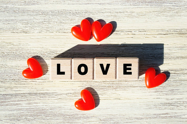 Word LOVE arranged from wooden letter blocks decorated with red hearts on a wooden background, top view. - Fotó, kép