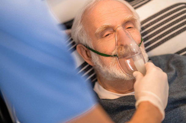 Experienced nurse conducting an oxygenation procedure on a bedridden man - Photo, image