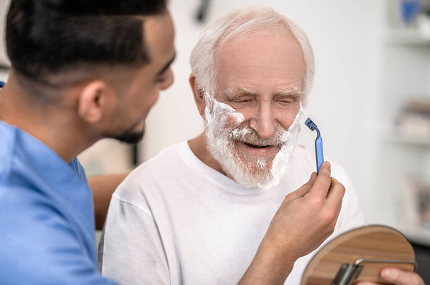 Caring volunteer giving a pleased old man a shave - Φωτογραφία, εικόνα