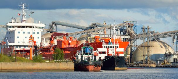 貨物港ターミナルに停泊する大型タンカーや小型船。背景にミネラル肥料の貯蔵とクレーン。貨物輸送、燃料および発電、産業、物流、商業 - 写真・画像