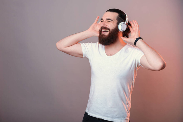 Joyful bearded man enjoys music and his earphones while dancing in a studio. - Zdjęcie, obraz