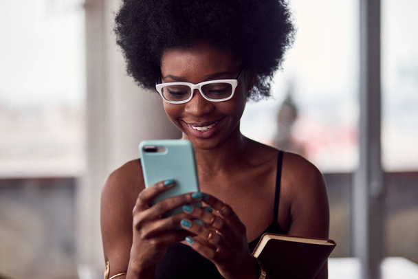 Cheerful african american woman holding smartphone and notepad. - 写真・画像