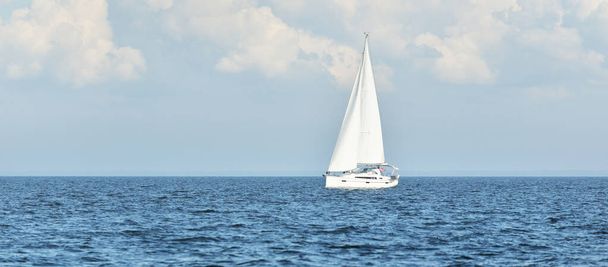 Sloop rigged yacht sailing in the Baltic sea. Dramatic sky after the storm, cumulus clouds. Transportation, travel, cruise, yachts racing, sport, recreation, leisure activity. Panoramic view - Photo, Image