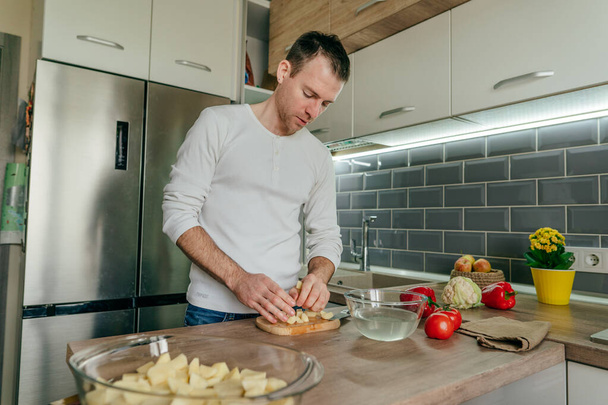 Un homme qui coupe des pommes de terre. Jeune homme cuisinant des légumes dans la cuisine préparant des pommes de terre. Concentration sélective. - Photo, image