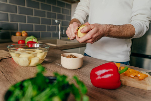 Man peeling potatoes. Unrecognizable man cooking vegetables in the kitchen. Close up of males hands preparing potato for cook. Selective focus. - Foto, afbeelding