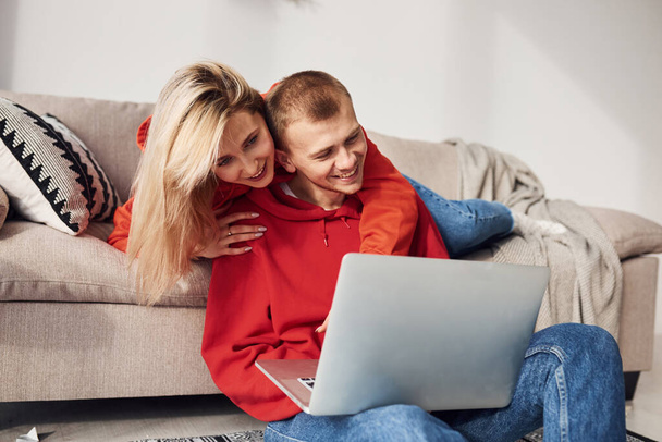 Using laptop that is on the legs. Young lovely couple together at home spending weekend and holidays together. - Photo, Image
