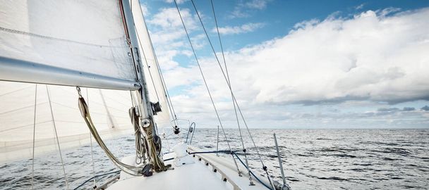 Açık bir günde açık denizde yelken açan beyaz yelkenli bir yat. Güverteden pruvaya bir manzara. Kümülüs bulutları. Ulaşım, seyahat, gezi, spor, eğlence, boş zaman aktivitesi, yarış, yelkenli yarışı - Fotoğraf, Görsel