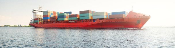 Containerschiff (168 Meter Länge) verlässt Hafen Terminal bei Sonnenuntergang. Ostsee. Güterverkehr, Logistik, globale Kommunikation, weltweite Schifffahrt, Wirtschaft, Wirtschaft, Industrie - Foto, Bild