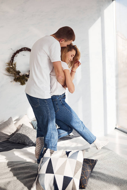Standing and embracing on bed. Young lovely couple together at home spending weekend and holidays together. - Valokuva, kuva