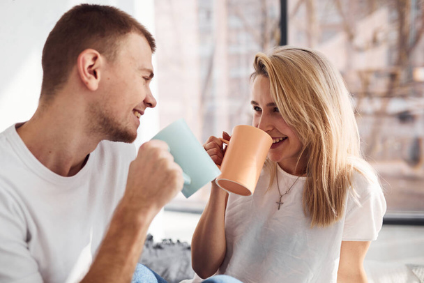 Young lovely couple together drinking warm tea at home spending weekend and holidays together. - Foto, afbeelding