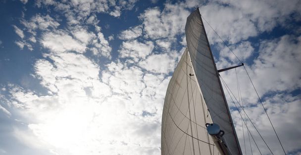 Sloop blanc gréé yacht naviguant dans la mer Baltique au coucher du soleil. Vue d'un cockpit au mât et voiles. Ciel dramatique. Transport, voyage, croisière, sport, loisirs, activité de loisirs, régate - Photo, image