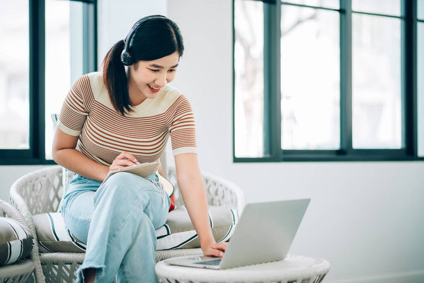 Asiatische junge Frau benutzt Laptop, um von zu Hause aus im Wohnzimmer zu arbeiten. - Foto, Bild