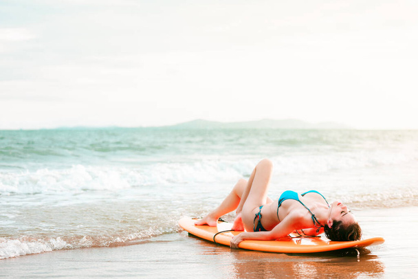 beautifull asian girl wearing bikini lying on surfboard and poses at the sand beach, in a tropical location, travel summer holiday relax in sea concept - Photo, image