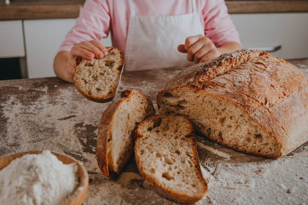 Unrecognizable little girl in apron holding a slice of homemade whole grain bread. Selective focus. - Photo, image