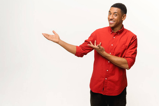 Handsome African-American young man in red shirt points palms aside isolated on white - Foto, Imagen