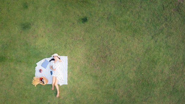 young asian woman lying relax on green glass and laptop with red coffee cup in the garden. Business technology and freelance  concept. aerial top view from drone - Foto, Imagem