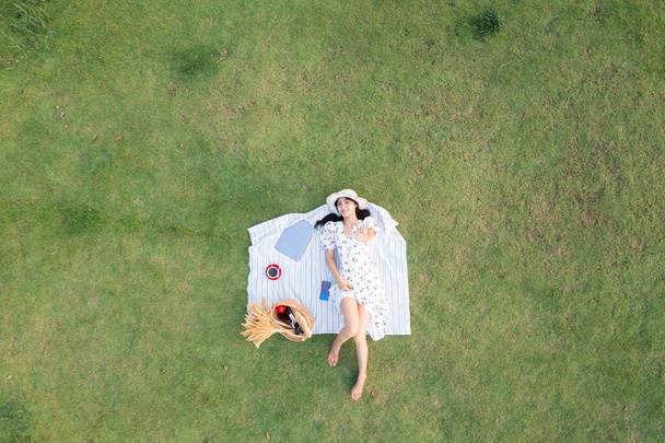 jeune femme asiatique couché se détendre sur verre vert et ordinateur portable avec tasse de café rouge dans le jardin. Technologie d'entreprise et concept freelance. vue aérienne du dessus depuis un drone - Photo, image