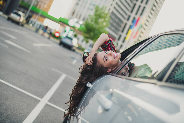 Portrait of attractive cheerful childish wavy-haired girl driving auto having fun throwing hair fooling on parking outdoors - Foto, afbeelding