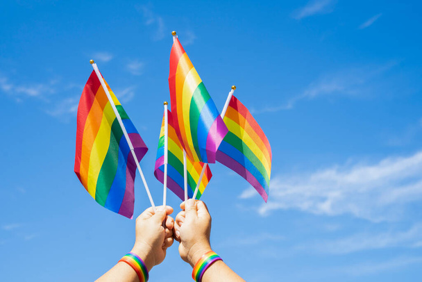радужные флаги Символ ЛГБТ-сообщества размахивается руками человека на фоне ясного голубого неба - Фото, изображение