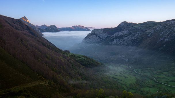 Landscape at dawn where we see the mountains and the valley of the Somiedo Natural Park in Asturias, Spain, with low clouds or mist in the green valley. - Photo, Image