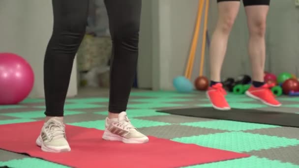 Sporty girl friends jump and do squats on yoga mats in gym - Metraje, vídeo