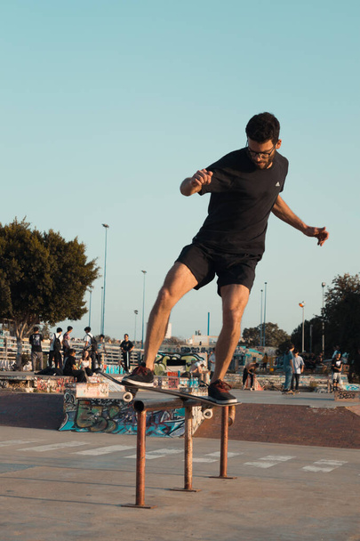 Skateboarder sliding on the railing of the skate park. Skater keeps his balance while performing tricks on the skateboard. Amateur skateboarder training outdoors. - Zdjęcie, obraz