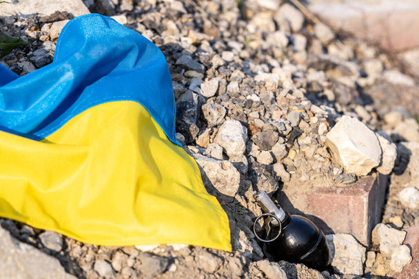 Ουκρανική σημαία και μια χειροβομβίδα που βρίσκεται μεταξύ ερείπια και ερείπια, Έννοια της επιθετικότητας και του πολέμου στην Ουκρανία - Φωτογραφία, εικόνα