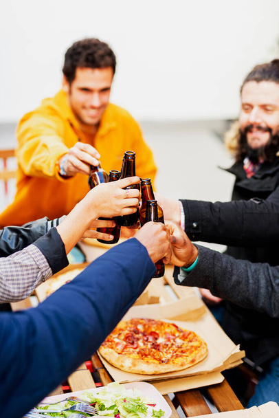 Groupe multi-ethnique d'amis trinquant avec des bières tout en dégustant un repas ensemble après le travail. - Photo, image