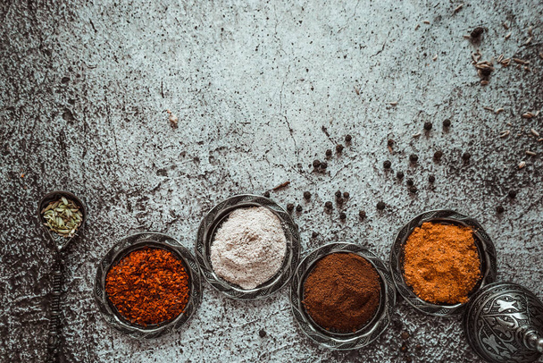 bright fragrant oriental spices, turmeric, curry, paprika, chili, black pepper, cloves, garlic in a Turkish metal dish on a gray background - 写真・画像