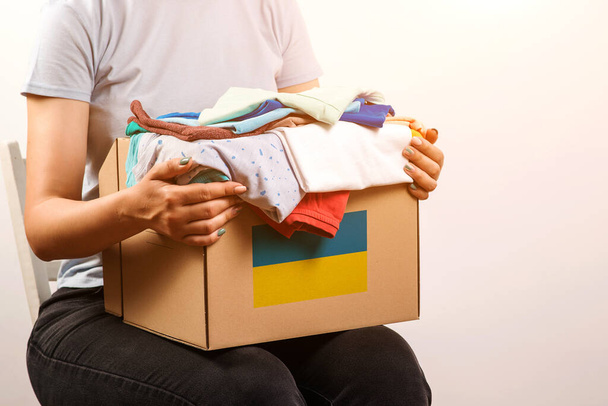 Box mit Kleiderspenden für ukrainische Kriegsflüchtlinge. Bleiben Sie bei der Ukraine. Freiwillige Cyrrying Box mit humanitärer Hilfe für ukrainische Flüchtlinge. Wohltätigkeit und Hilfe für arme und bedürftige Menschen. - Foto, Bild