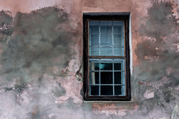 Ένα μικρό παράθυρο με σιδερένια σχάρα και ένα παλιό ξεφλουδισμένο τοίχο του σπιτιού. - Φωτογραφία, εικόνα