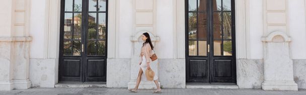 side view of trendy woman walking along white building with black doors, banner - Foto, Imagem