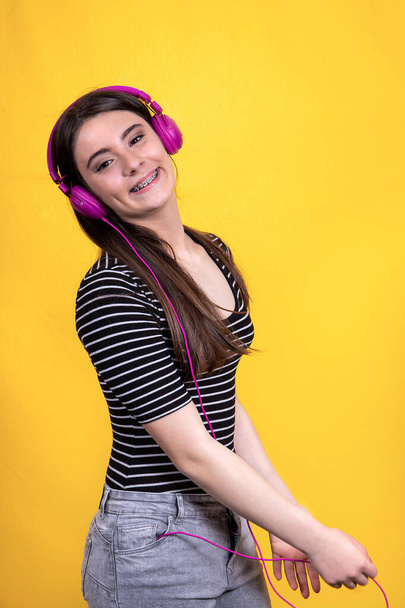 Portrait of beautiful smiling girl with long hair. The young woman wears jeans and a striped t-shirt and uses headphones to listen to music. - Foto, immagini