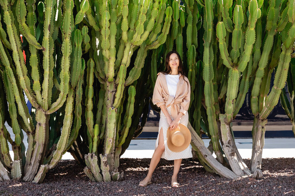piena vista lunghezza della donna sorridente in piedi con cappello di paglia vicino cactus enormi - Foto, immagini