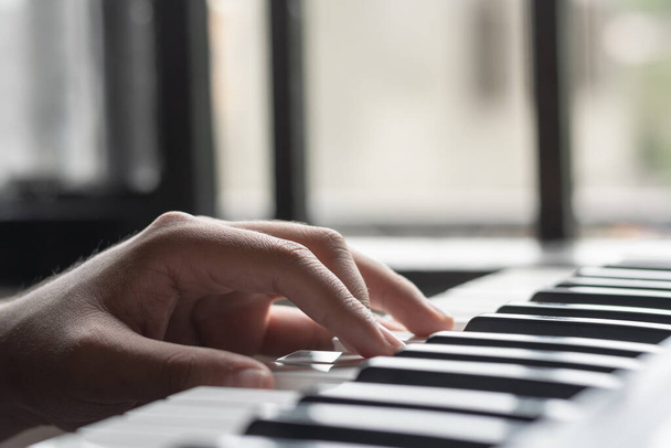 detailed view of a latin man's left hand, with his fingers on the keys of a piano playing bass notes and creating melodies on his synthesizer. practicing new sounds. - Foto, afbeelding
