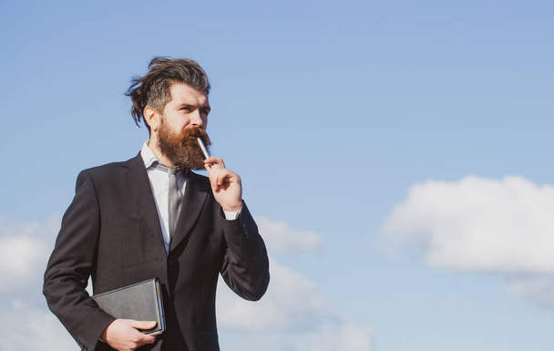 Business man with sky. Business man is thinking about something with pencil. Business dreams. Thoughtful young man in shirt and tie holding note pad and pen. - Photo, image