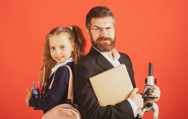 Elementary pupil with teacher in red studio, isolated. Portrait of funny school girl and tutor with school supplies. Happy teacher and student girl on red. - Foto, Imagen